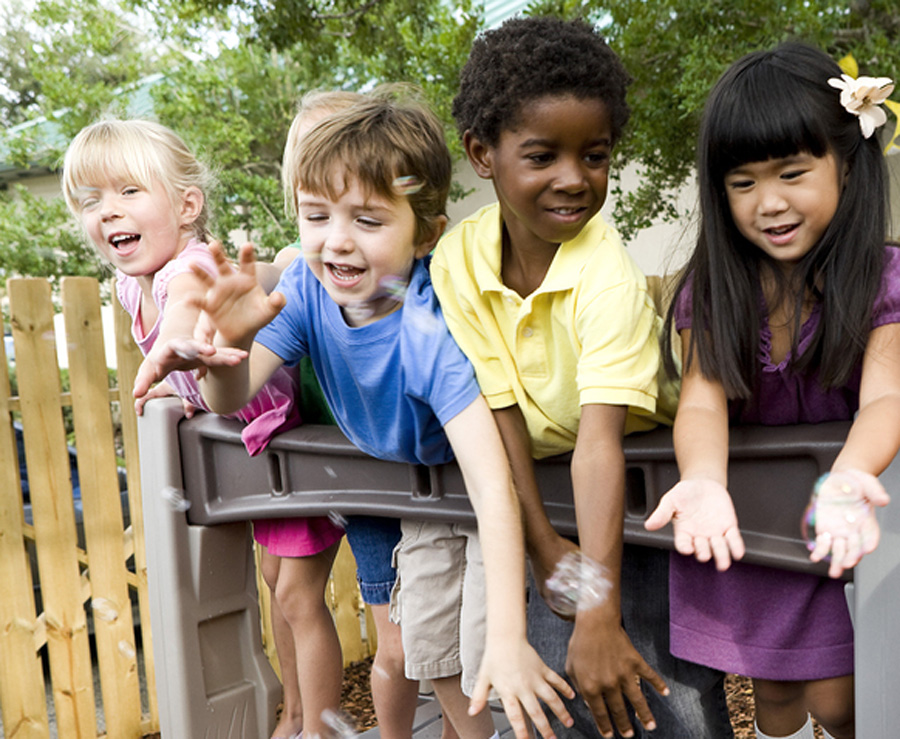 Preschool children playing on playground with teacher